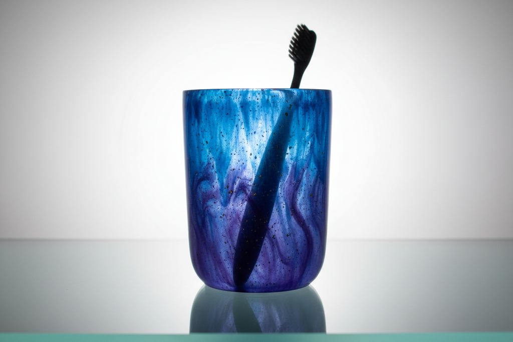 Backlit resin tumbler on white surface showing internal color depth with toothbrush silhouette inside