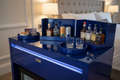 Three cobalt lacquer trays nested open on hotel minibar credenza displaying shot glasses, spirit bottles, and base tray under warm ambient light