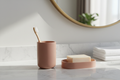 Dusty rose resin tumbler with toothbrush and matching soap dish on white marble hotel vanity