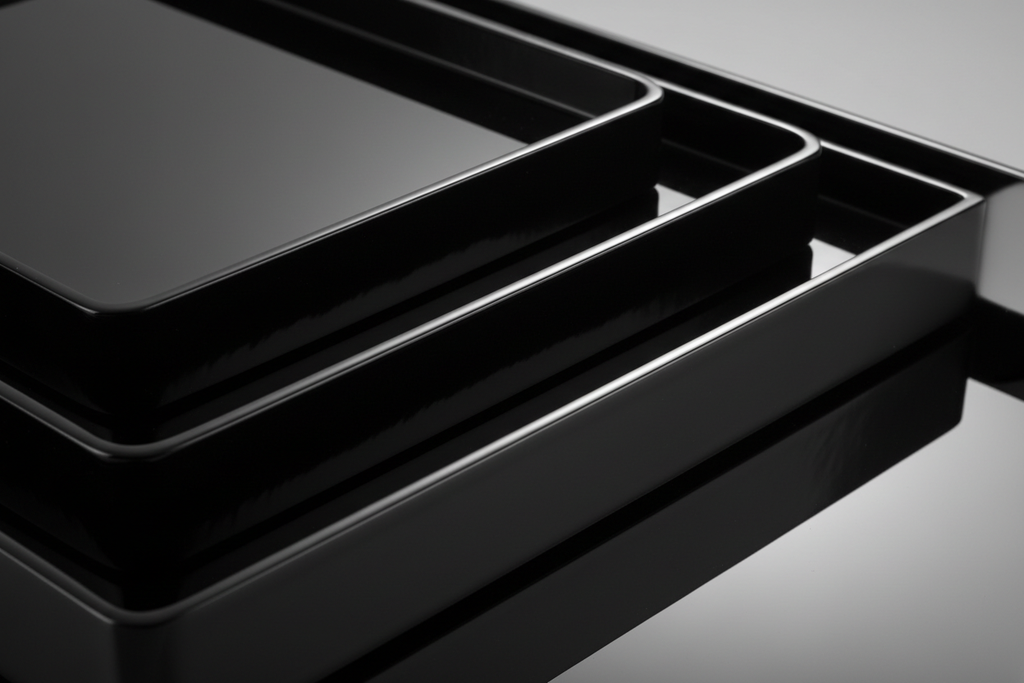 Side angle close-up of three lacquer trays stacked nested showing rim heights with studio light reflecting across all three high-gloss surfaces