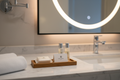 Small teak amenity tray on hotel bathroom vanity with soap, lotion bottles, and branded card